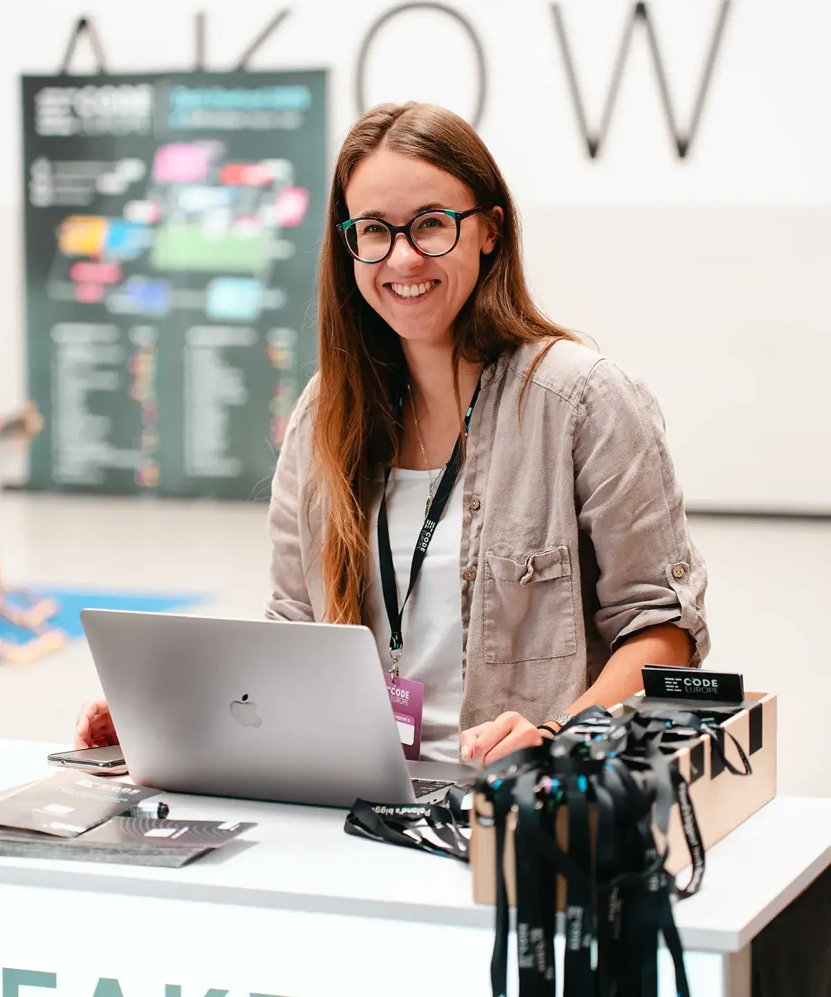 Młoda kobieta uśmiecha się w obiektyw aparatu i robi coś na komputerze.